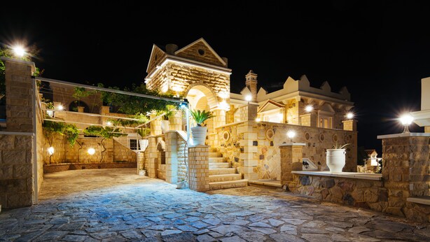 A stone courtyard with a stone staircase leading to a building with a pitched roof and arched windows. - Anesis Family Villas (Faistos)