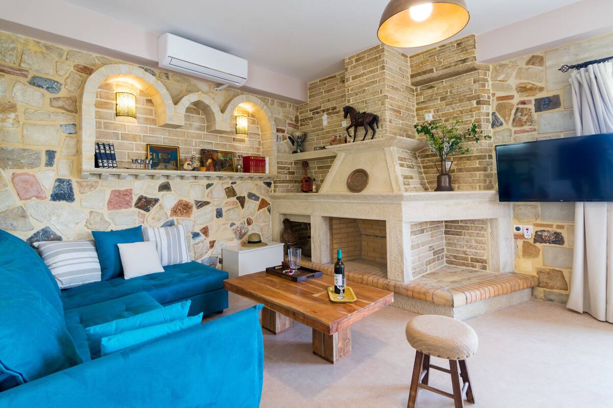 A cozy living room with a stone fireplace, a blue sofa, a wooden coffee table, and a mounted television.