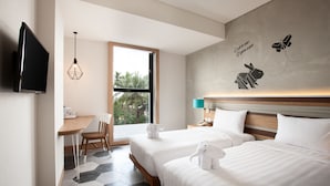 Quarto de hotel com duas camas, uma mesa de trabalho, televisão e janela com vista para árvores.