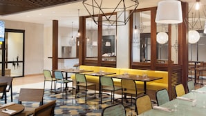 Uma sala de jantar moderna com luminárias pendentes geométricas, um assento em cabine amarelo e piso estampado.