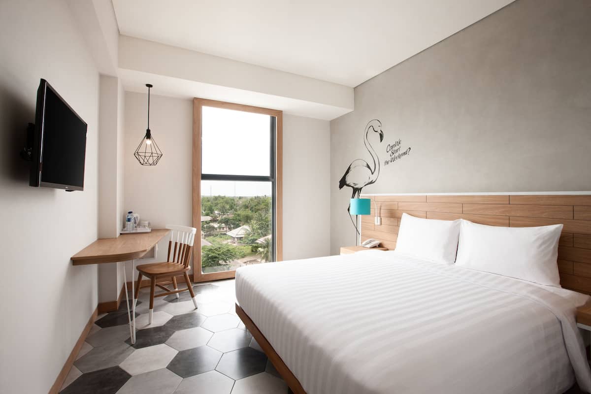 A modern hotel room with a large bed, a desk with a chair, a TV, and a view of the outdoors.