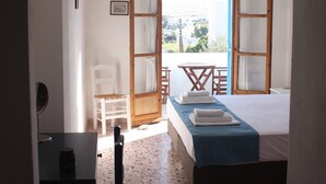 A room with a bed, a table, and a chair. There is an open door leading to a balcony with a view of the city. - Meltemi Studios and Apartments (Paros)
