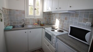 A kitchen with white cabinets, a sink, a stove, and a microwave. - Meltemi Studios and Apartments (Paros)