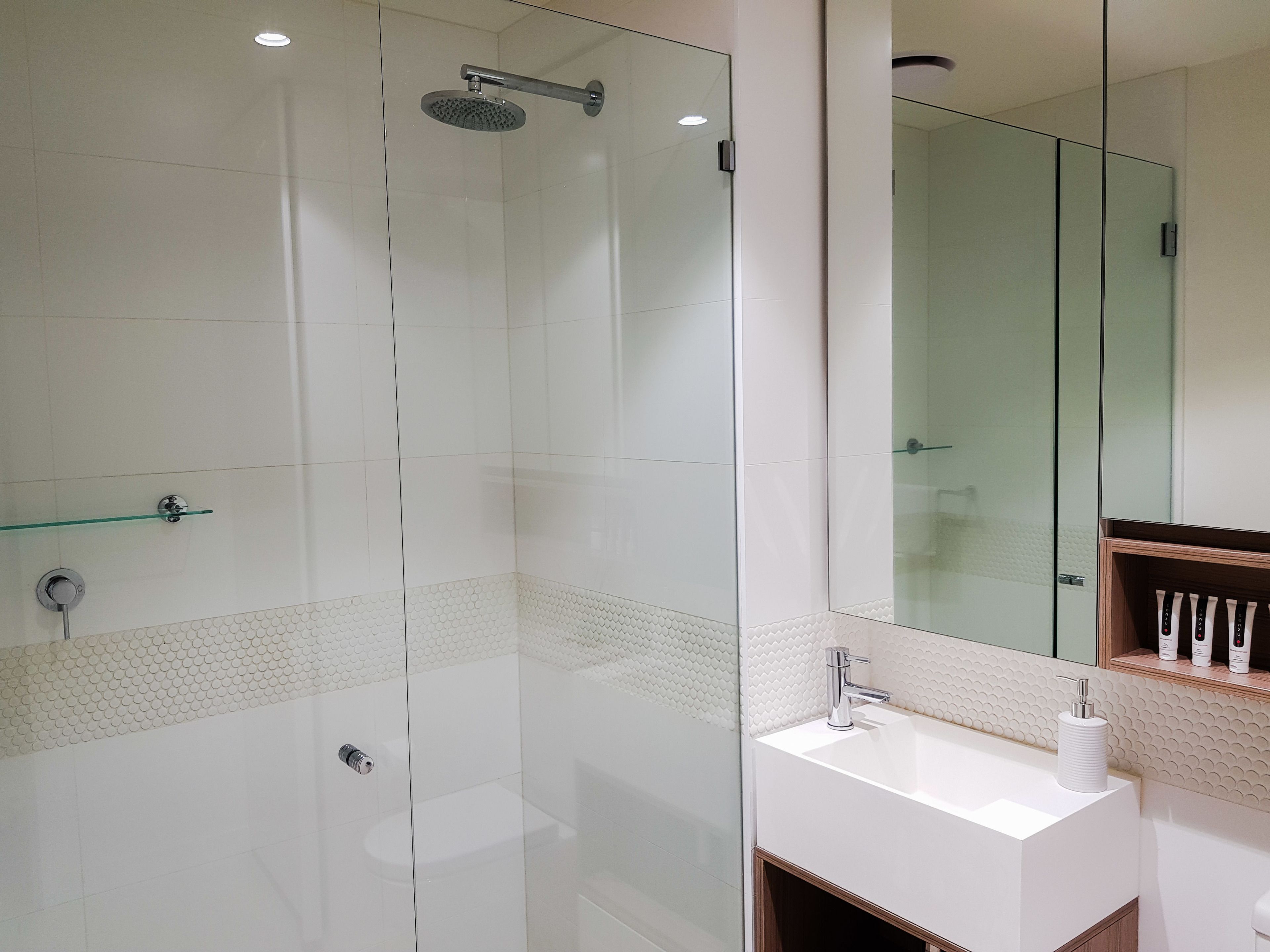Un baño moderno con cabina de ducha de vidrio, un lavabo blanco y un espejo sobre él.