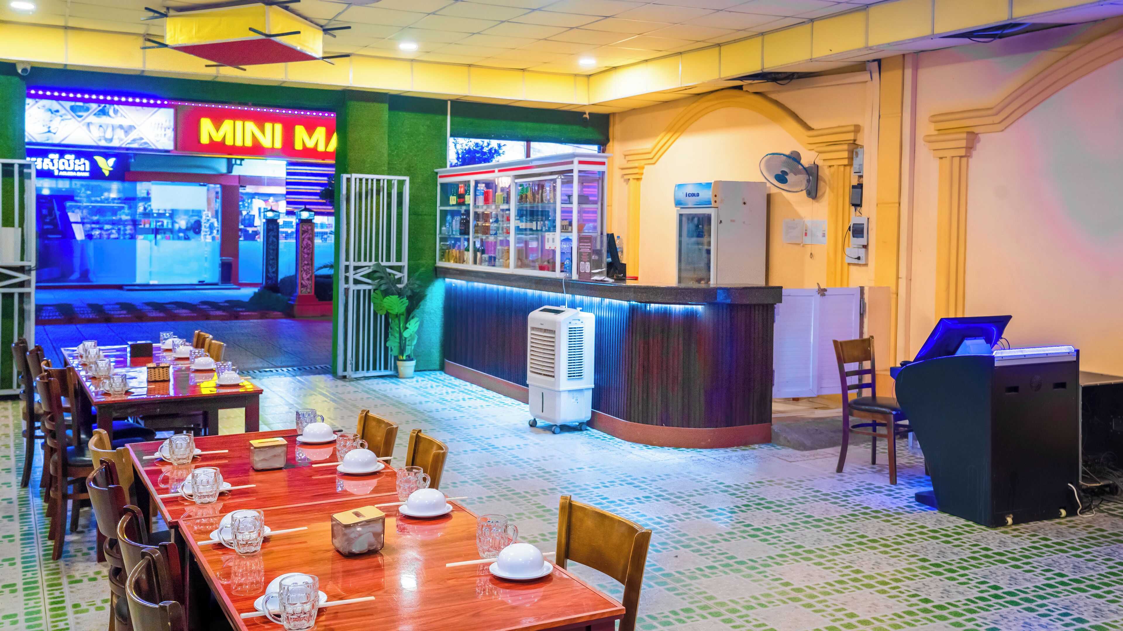 A restaurant with a long counter, tables set with plates and glasses, and a neon sign in the background.