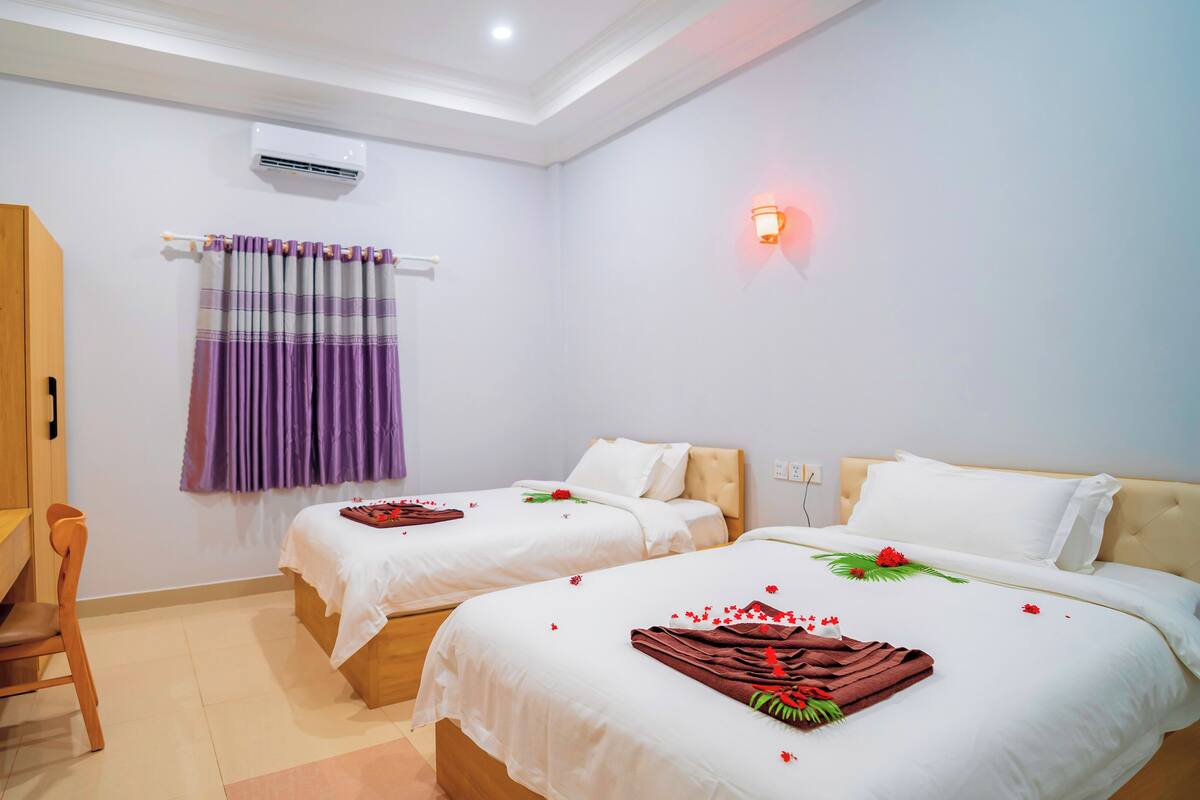 Une chambre d’hôtel avec deux lits, un bureau, une chaise, un appareil de climatisation et un luminaire fixé au mur.