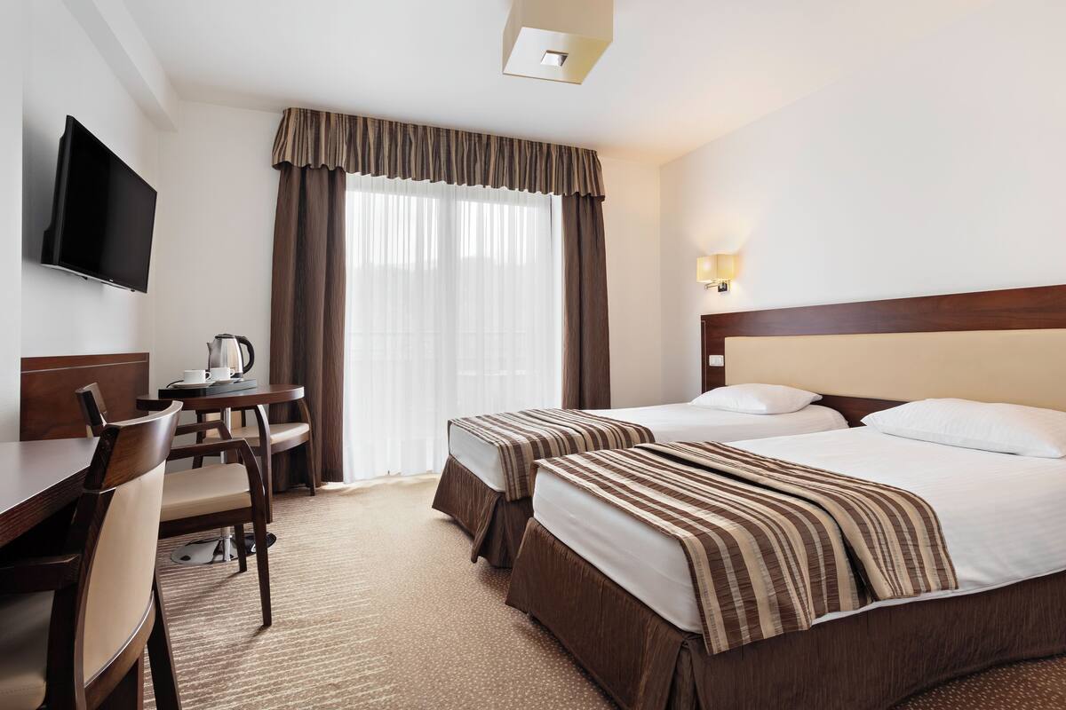 A hotel room with two beds, a desk with a chair, a television, and a window with curtains.