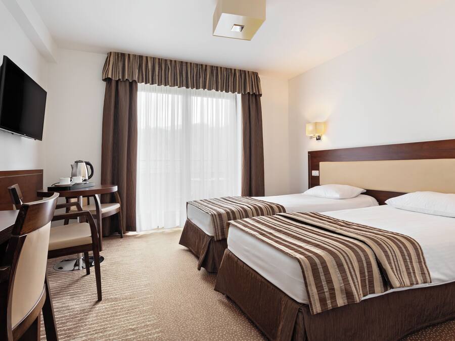 A hotel room with two beds, a desk with a chair, a television, and a window with curtains.