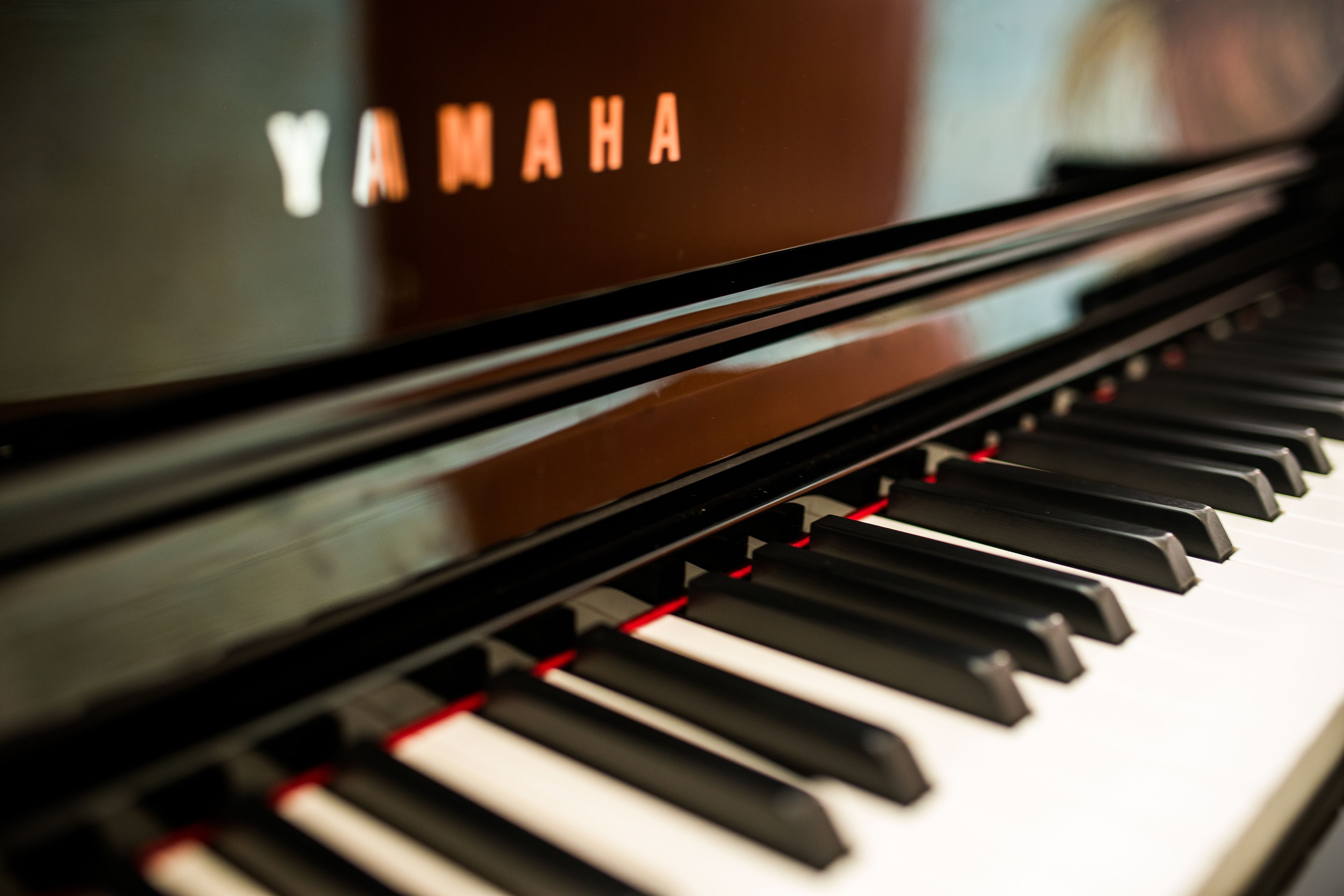 Primer plano de un piano Yamaha con un acabado negro brillante y detalles rojos en las teclas.