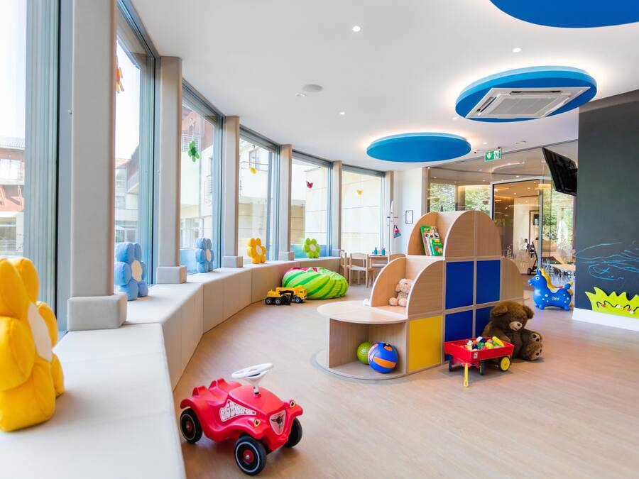 Ein moderner Spielbereich für Kinder mit großen Kuscheltieren, einem Spielhäuschen und einem roten Spielzeugauto.