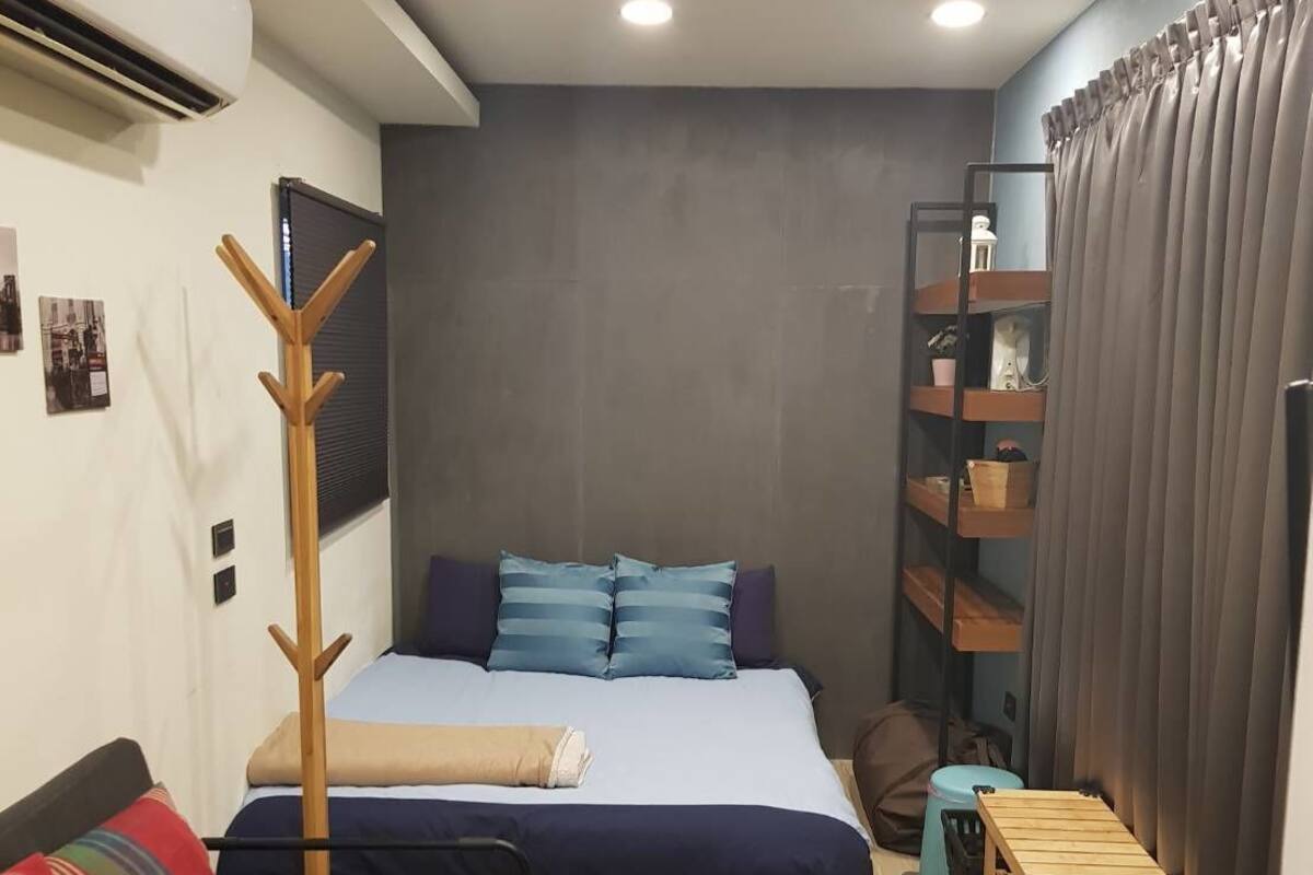 A compact bedroom with a bed, a sofa, a wooden bench, a shelf unit, and a curtain.