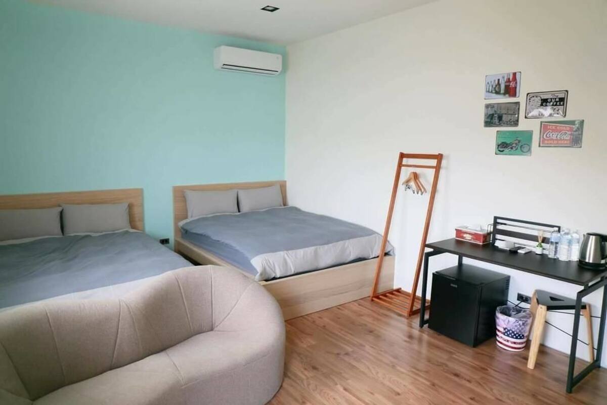 A room with two beds, a desk, and a chair. There is an air conditioning unit on the wall and a small trash bin.