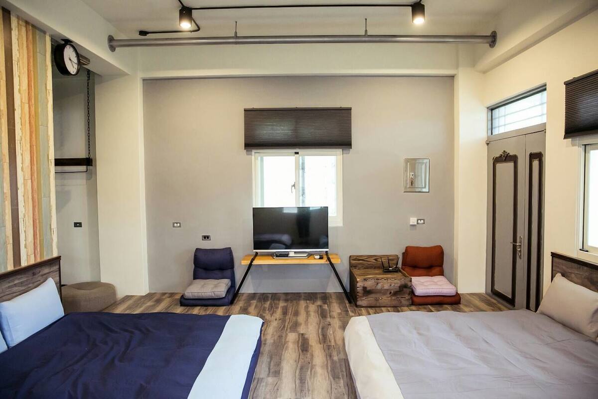 A modern hotel room with two beds, a TV, a small seating area, and a large window.