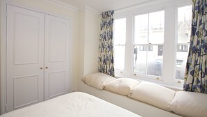 A bedroom with a bed, two windows with curtains, and a wardrobe. - A Place Like Home - Comfortable Apartment in Paddington (London)
