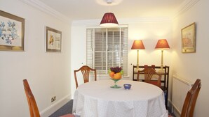 A dining area with a round table, chairs, a fruit bowl, and two lamps. - A Place Like Home - Comfortable Apartment in Paddington (London)