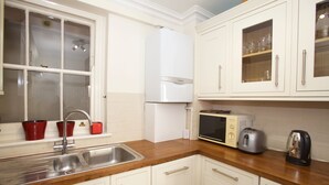A kitchen with white cabinets, a stainless steel sink, a microwave, a toaster, and a kettle. - A Place Like Home - Comfortable Apartment in Paddington (London)