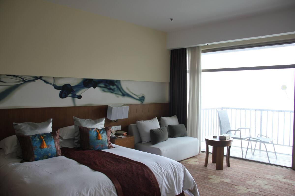 Une chambre d’hôtel avec un grand lit, un canapé, une petite table et un balcon avec des chaises.