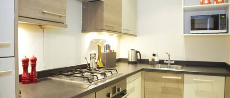 A modern kitchen with a gas stove, oven, and microwave. There are cabinets, a sink, and a countertop with various kitchen items.