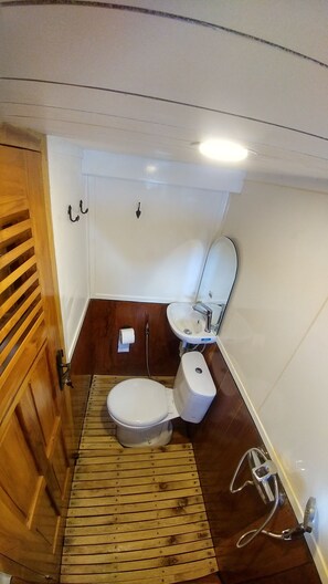 A compact bathroom with a wooden floor, a white toilet, and a sink. - LaUnua (Labuan Bajo)