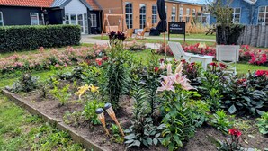 Un jardín con diversas flores y plantas, un columpio de madera y un letrero de café.