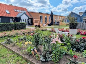 Un jardin agrémenté de diverses fleurs et plantes, une balançoire en bois et un panneau indiquant l’emplacement d’un café.