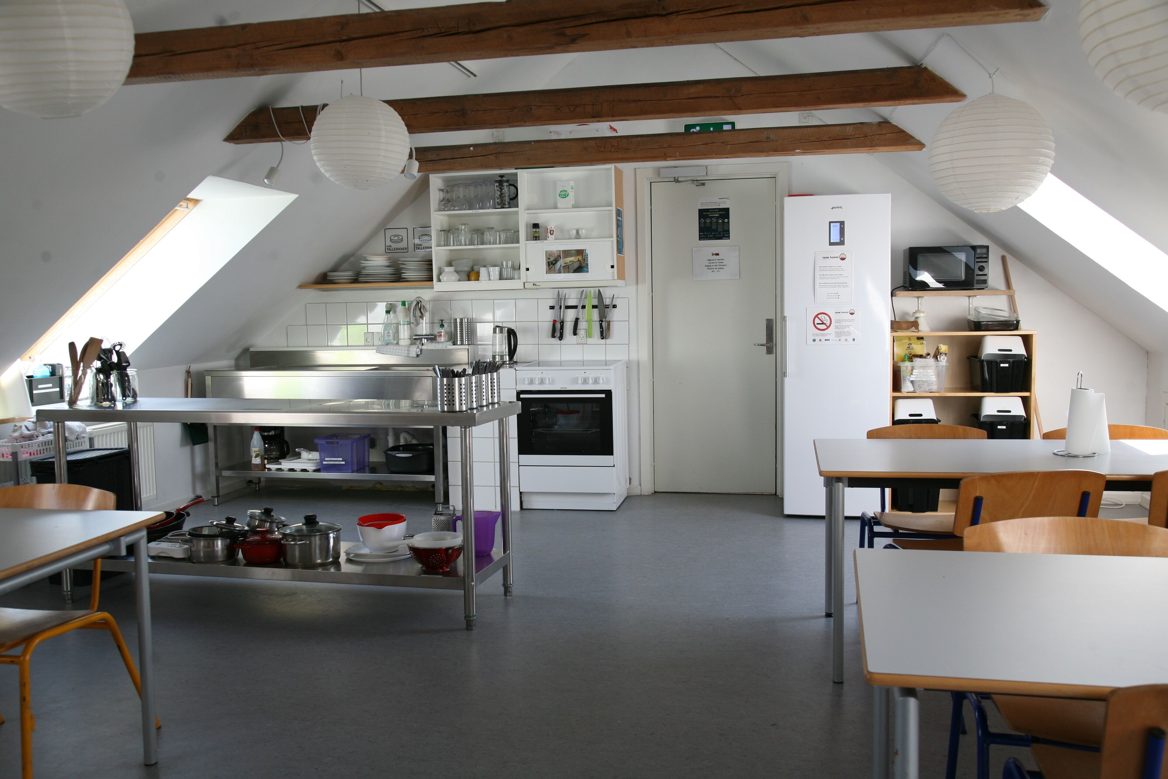A kitchen with a stove, microwave, and various utensils. There is a dining area with tables and chairs.