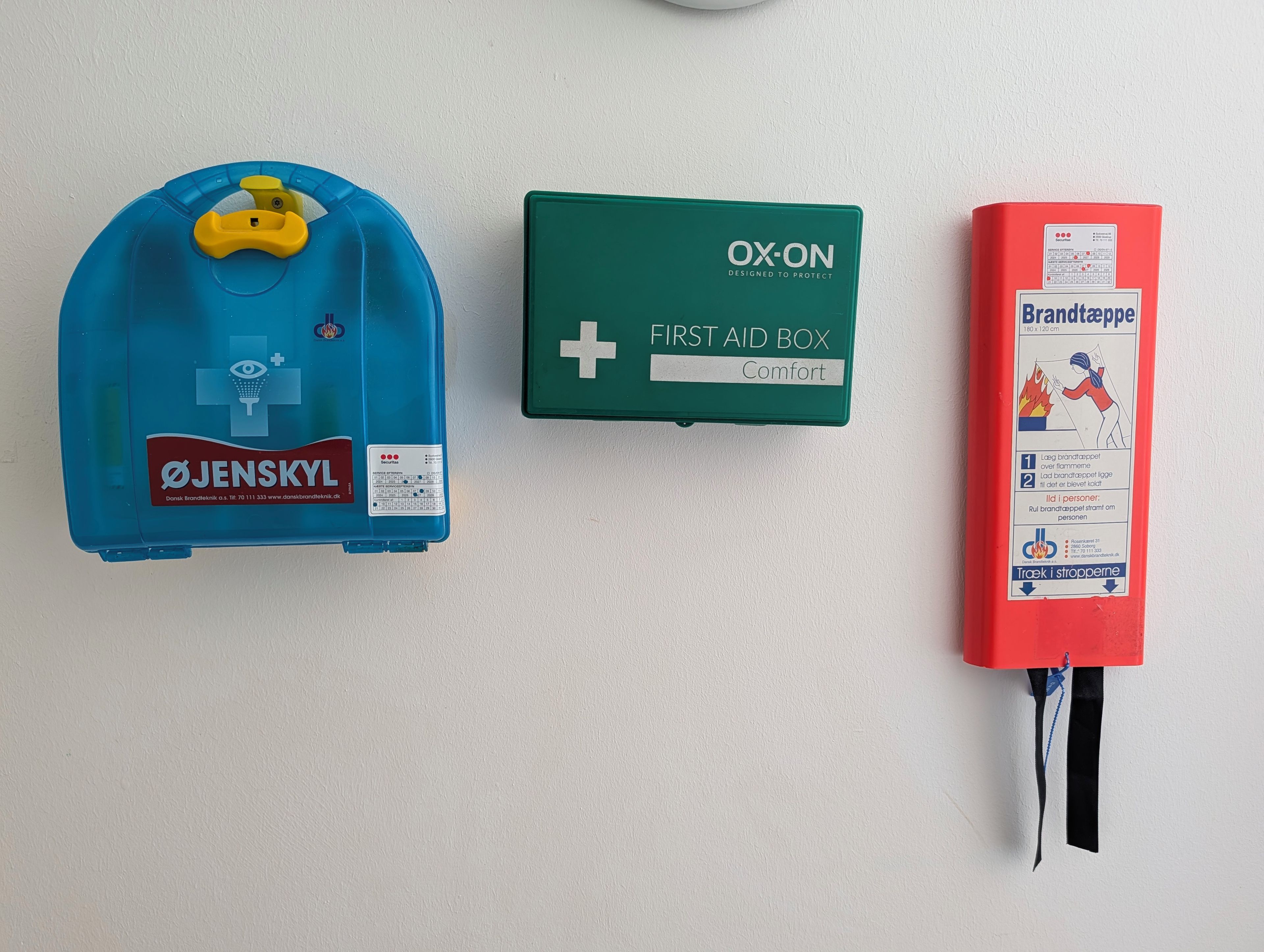 Trois éléments d’équipement d’urgence : une bouteille d’oxygène bleue, une trousse de premiers secours verte et un extincteur rouge.