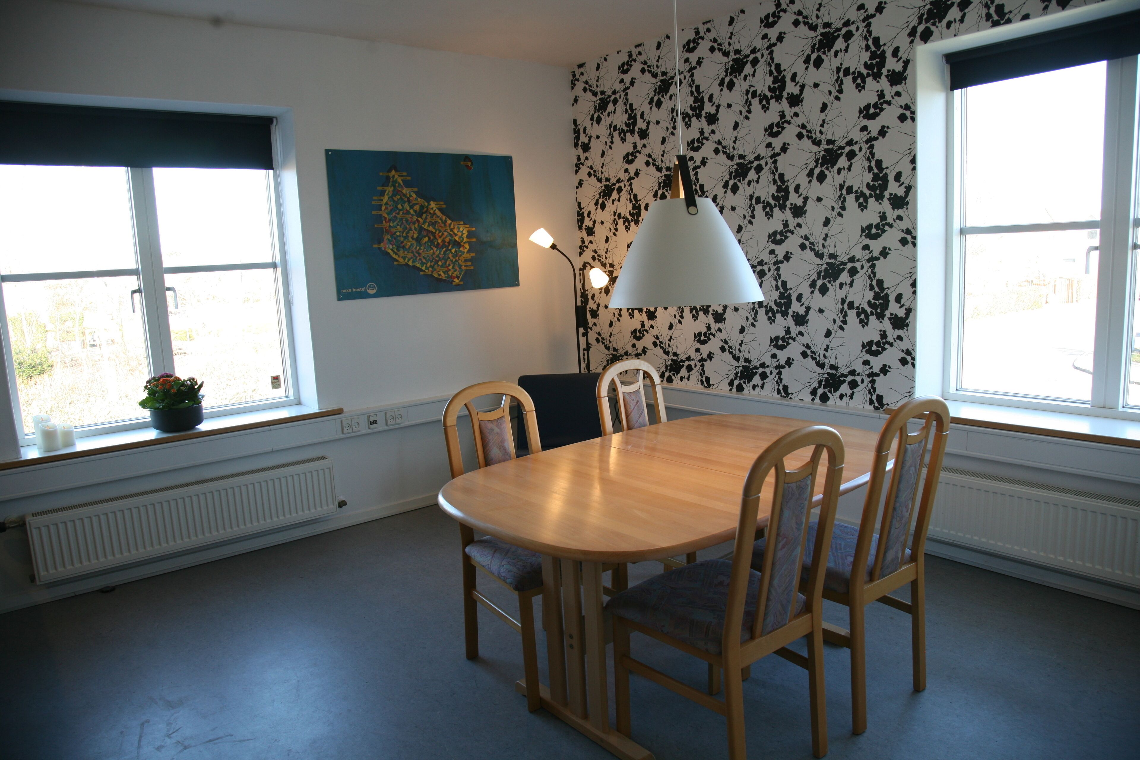 Een eethoek met een houten tafel en stoelen, een potplant en een muur met een bloemenpatroon.