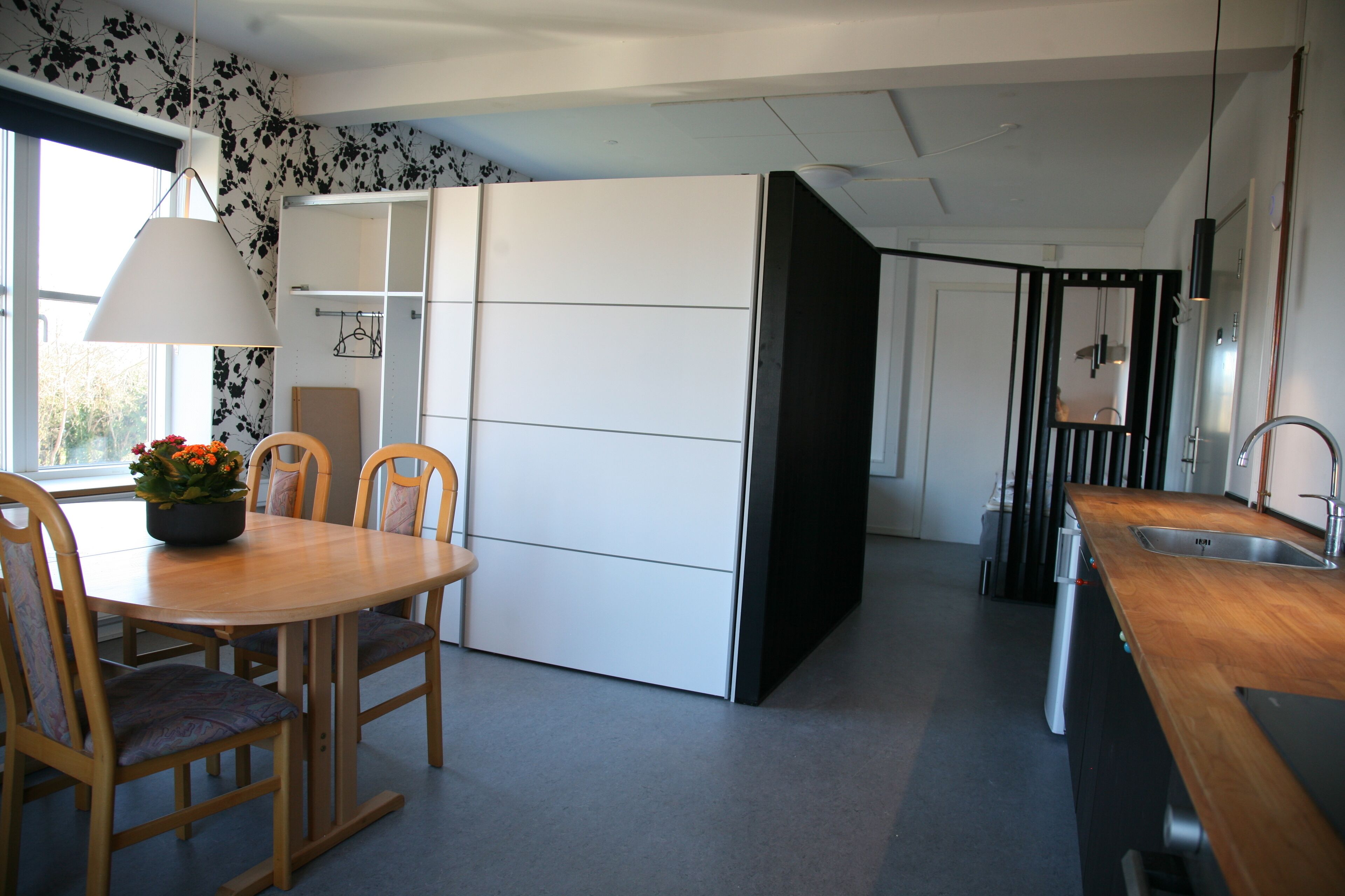 A modern kitchen with a dining area, featuring a wooden table and chairs, a built-in oven, and a black countertop with a sink.