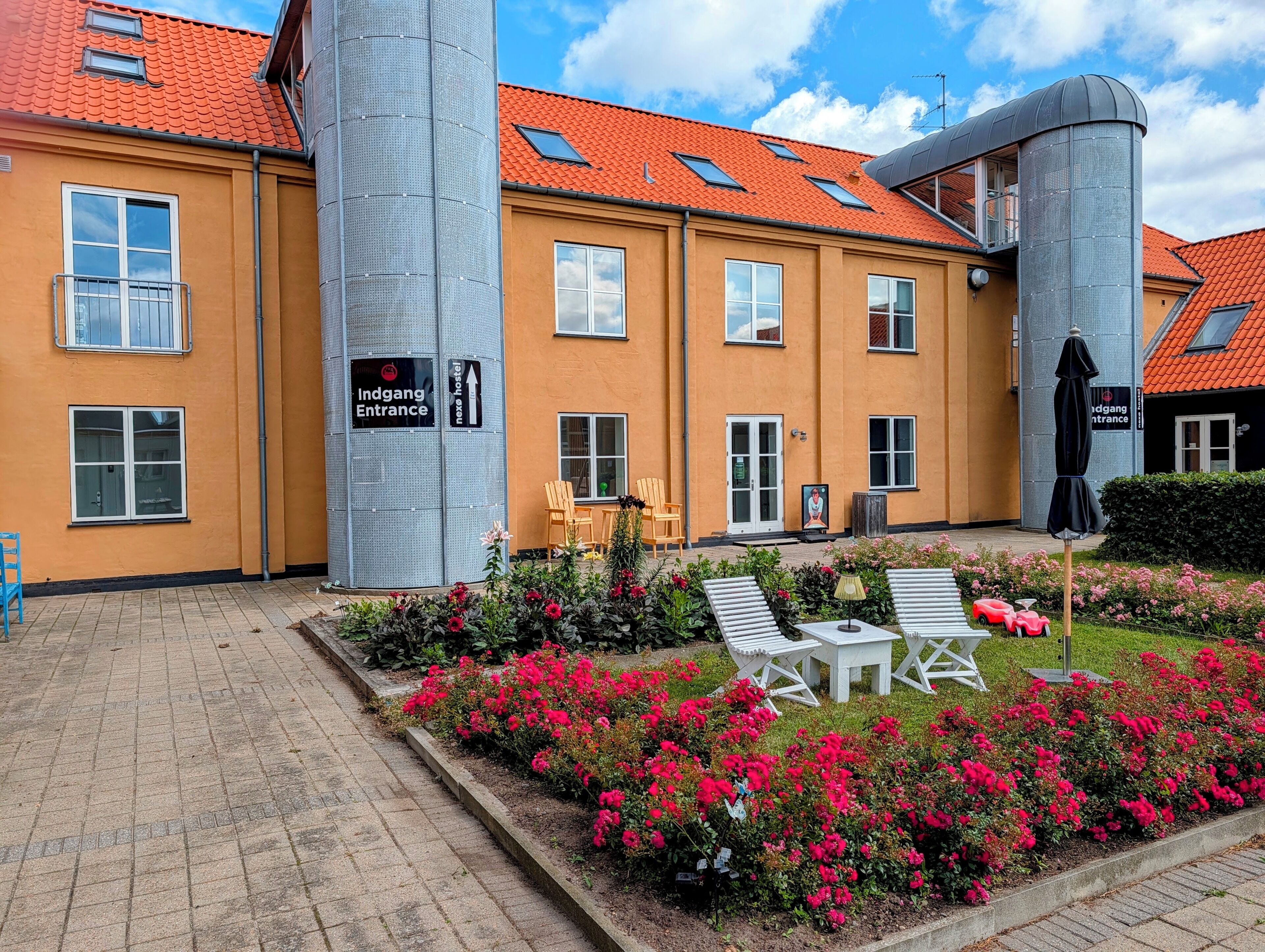 Ein Hotel mit gut erkennbarer Schilderung, Sitzgelegenheiten im Freien und einem Blumengarten.