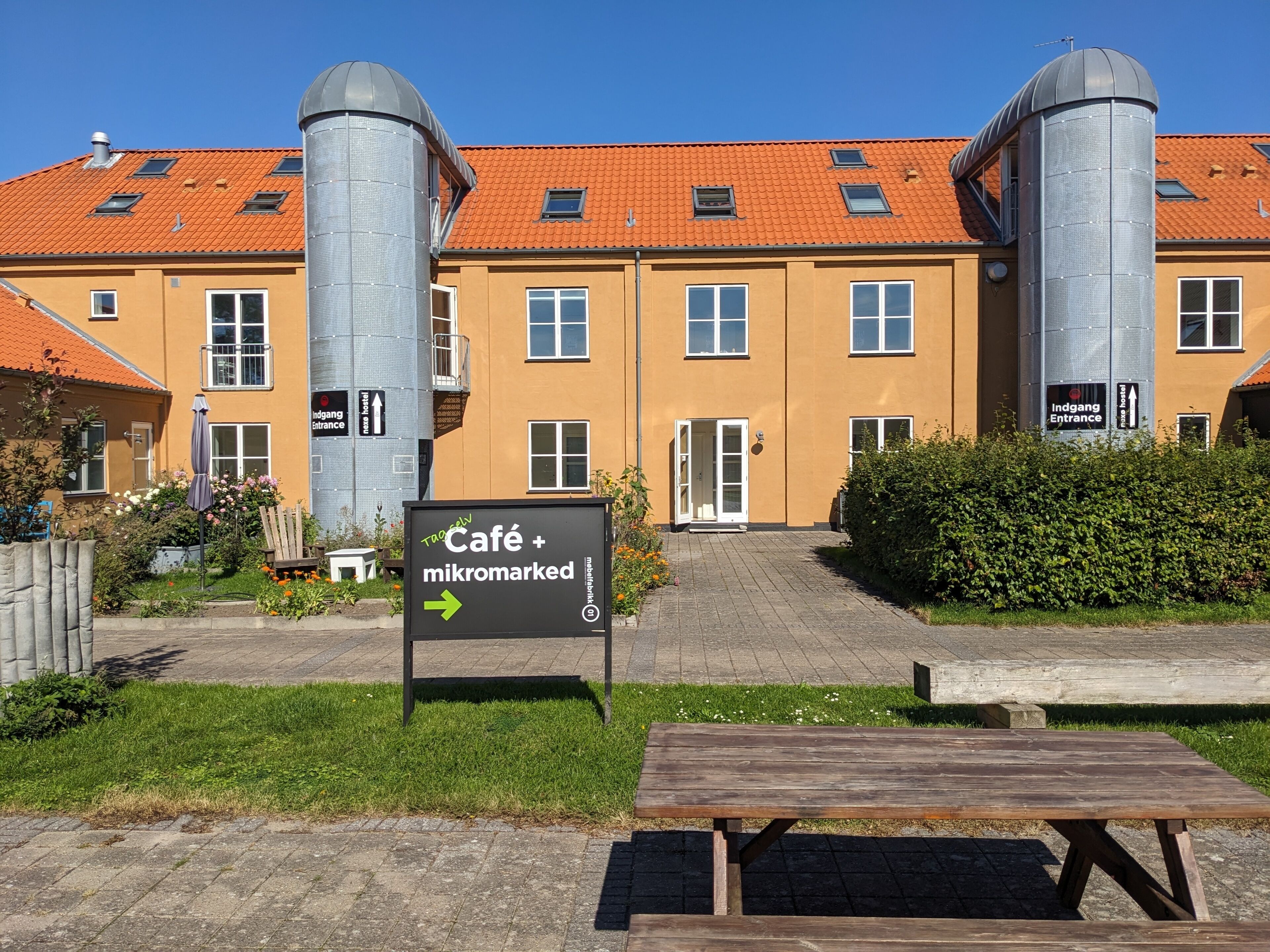 A building with a café and mikromarked sign, a wooden bench, and a grassy area.