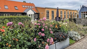 Un quartier résidentiel avec une maison dont le toit est recouvert de tuiles rouges, un jardin agrémenté de différentes fleurs et une clôture en bois.