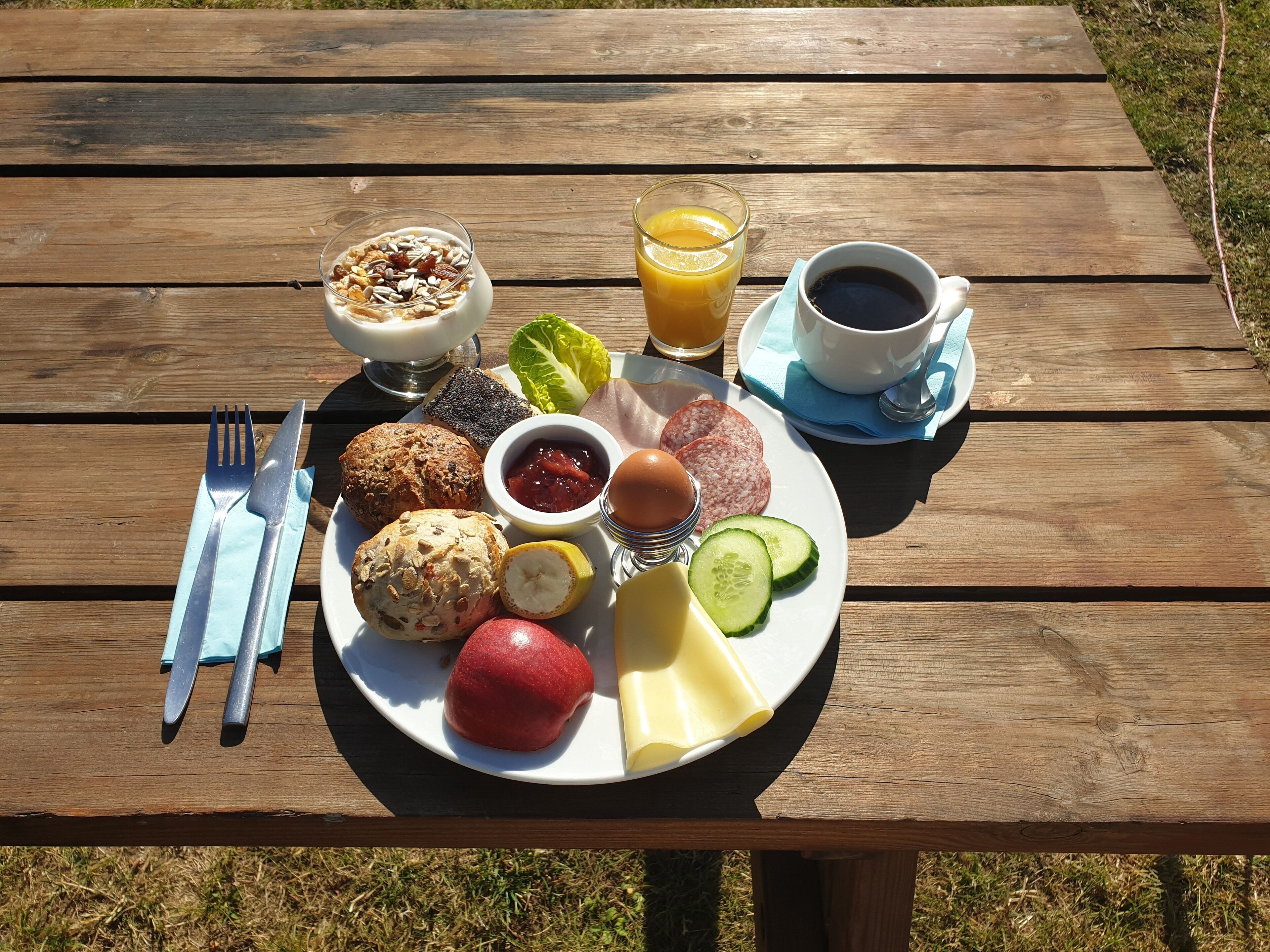 Una mesa de picnic con un plato de comida que incluye pan, huevos, fruta y una bebida.