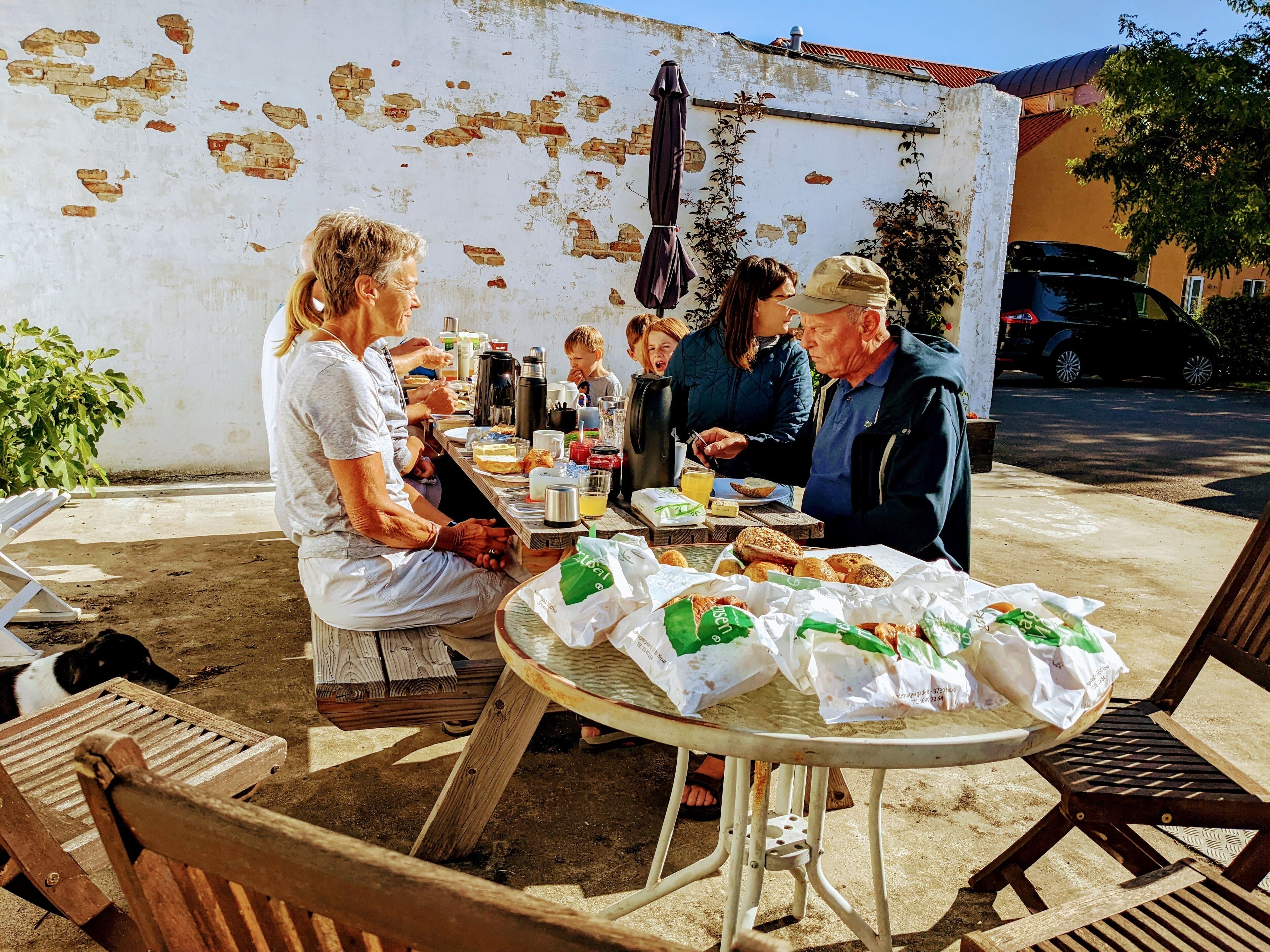A round outdoor table with a white tablecloth, surrounded by wooden chairs.
