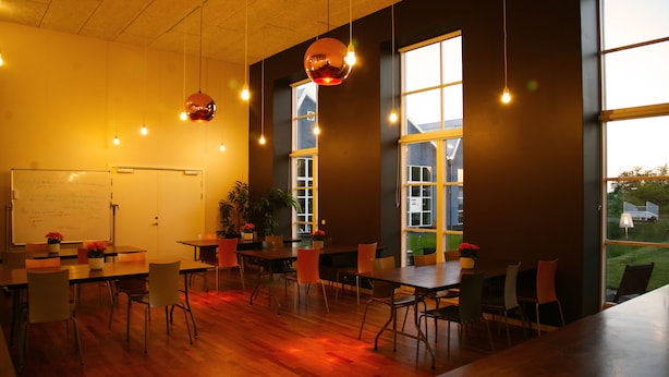 Une salle de conférence équipée d’un tableau blanc, de tables, de chaises et de grandes fenêtres.