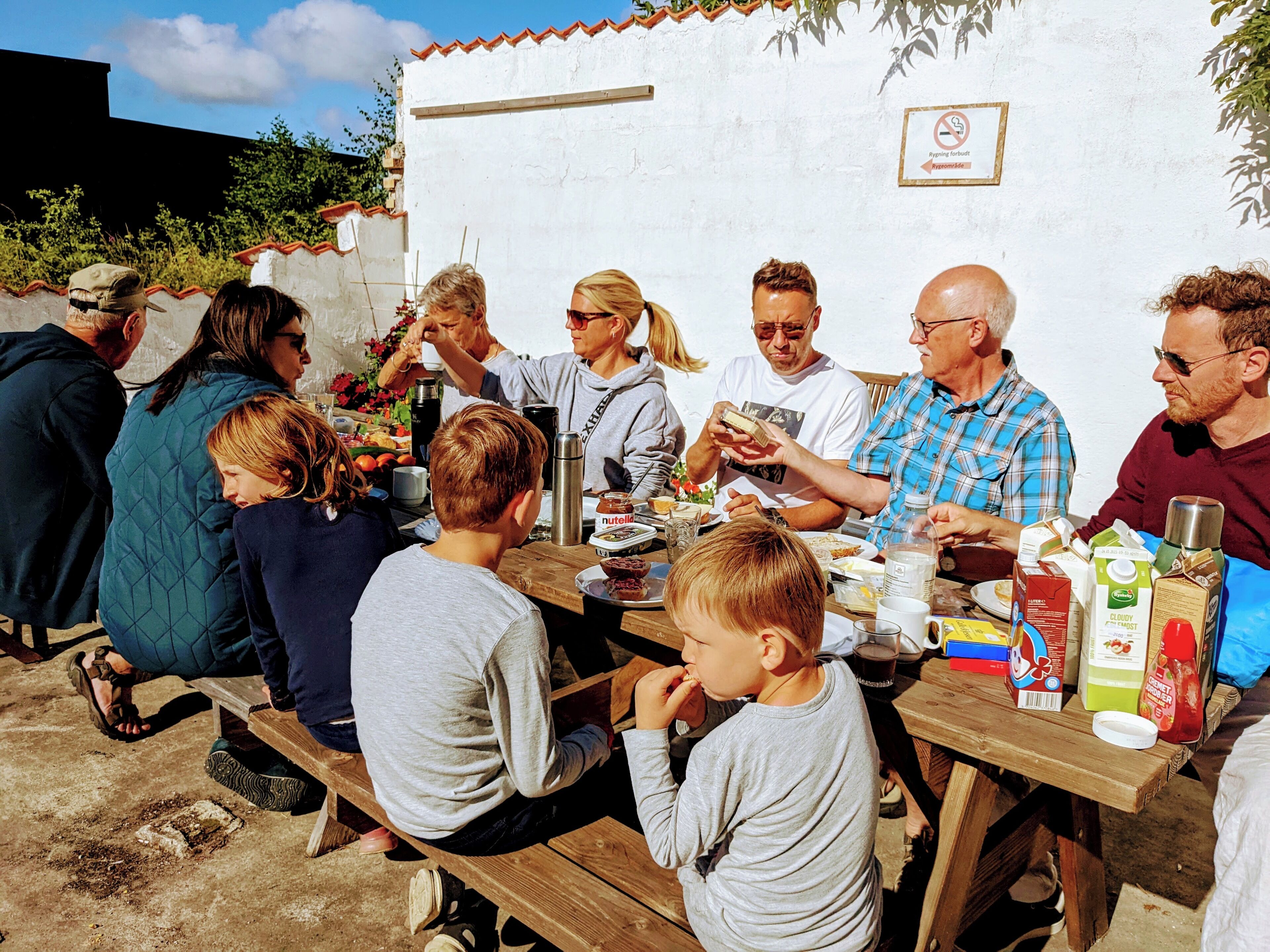 A group of people seated at a wooden table outdoors, with food and drinks.