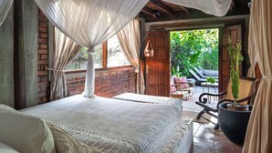 A bedroom with a canopy bed, a view of the garden, and a wooden door leading outside.