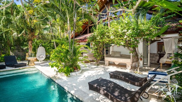 A poolside area with lounge chairs, a small pool, and lush tropical vegetation.