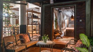 A cozy outdoor seating area with wooden benches and a small round table, surrounded by brick walls and potted plants.