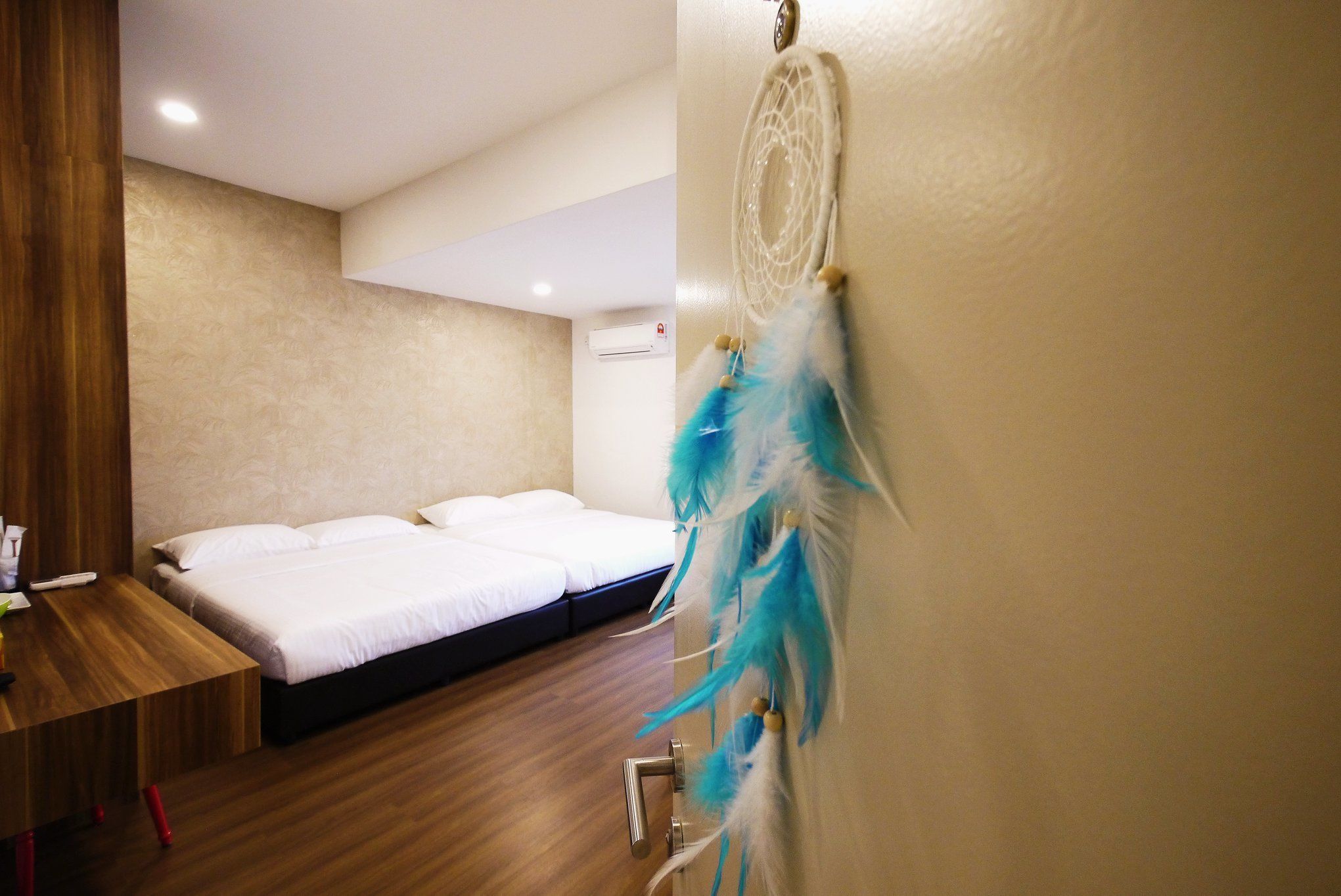 A hotel room with a wooden floor, a bed with white bedding, a wooden nightstand, and a dreamcatcher on the wall.