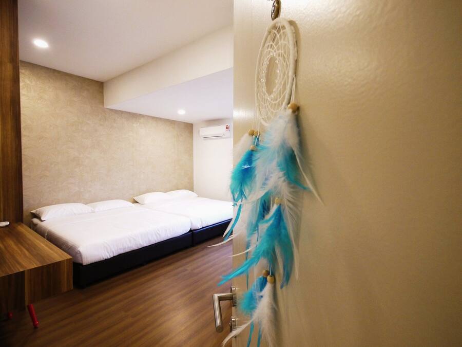 Una habitación de hotel con suelo de madera, una cama con ropa blanca, una mesita de noche de madera y un atrapasueños en la pared.