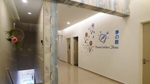 A hotel lobby with a reception desk, a seating area with patterned chairs, a decorative wall with a logo, and a tiled floor. - Dreamcatchers Home (Kuantan)