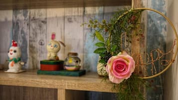 Una estantería de madera con diversos objetos decorativos, incluyendo una figurita de muñeco de nieve, un conejo, un frasco pequeño y una rosa rosa en un jarrón.