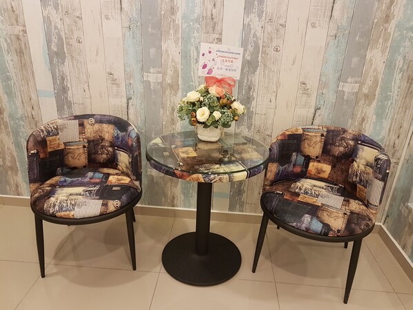 Dos sillones de estilo patchwork con una mesa de vidrio en el centro, un pequeño jarrón con flores y un cartel en la pared.