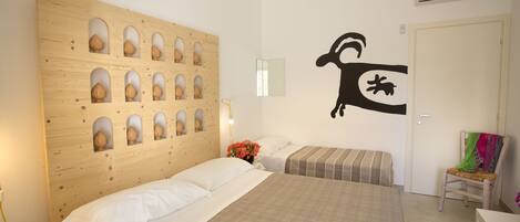 Habitación de hotel con dos camas, cabecera de madera, aire acondicionado montado en la pared y una silla pequeña con una manta colorida.