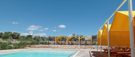 A swimming pool with a stone deck, yellow canopies, and picnic tables.