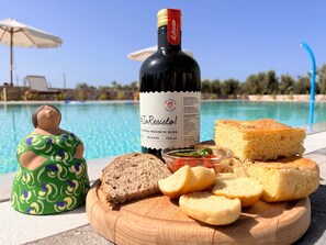 A bottle of wine, bread, and a figurine by a poolside. - TerreAmare Agriturismo (Nardò)