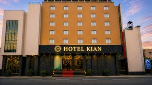 Un hotel con un llamativo letrero que dice 'HOTEL KIAN', varios pisos y un letrero de estacionamiento que indica aparcamiento cercano.