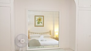 Ein Schlafzimmer mit einem Bett, einem Nachttisch, einem Spiegel und einem Ventilator.