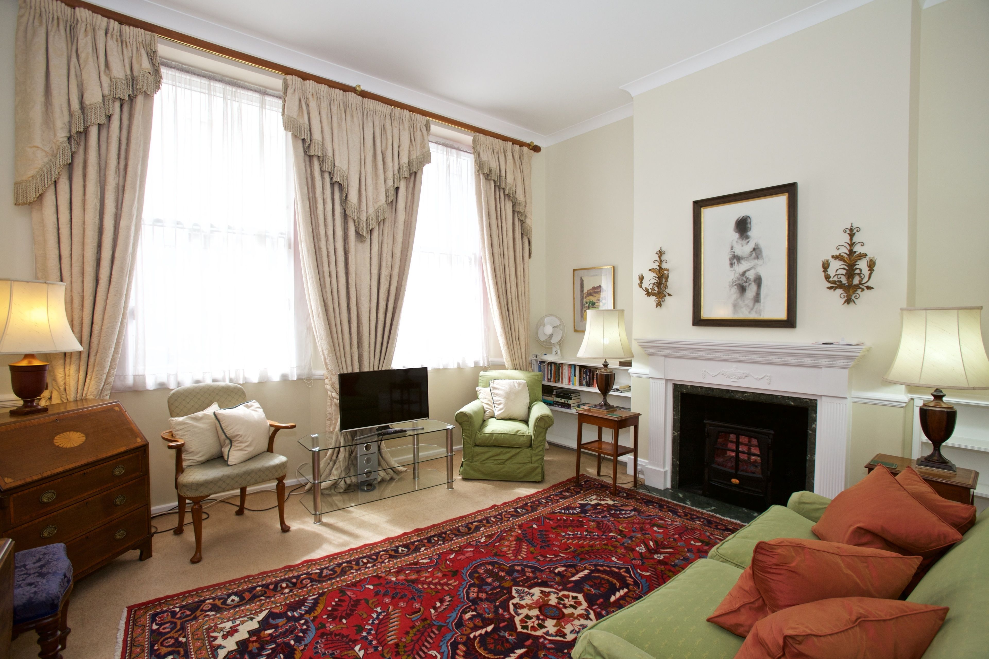 A living room with a green sofa, a red patterned rug, a fireplace, and a television.